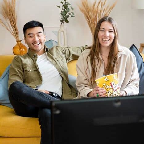 Multiracial couple of friends watching movies at home. Multiracial couple of friends watching movies at home, sitting in living room eating popcorn.